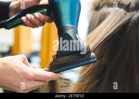 Master donna parrucchiere asciuga i capelli della ragazza con un asciugacapelli e pettini dopo il lavaggio nel salone di bellezza Foto Stock