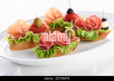 Tartine di baguette tenue con lattuga, salame o prosciutto di Parma, pomodori, mozzarella e olive. Piatto assortito di prelibatezze per la festa. Foto Stock