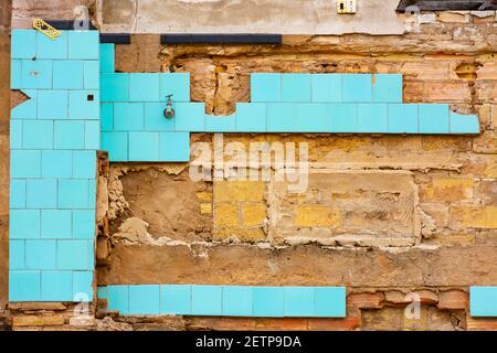 Resti della parete interna di una casa in un edificio in rovina, con pezzi di piastrelle blu e parti della parete grezza Foto Stock