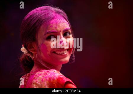 UNA GIOVANE DONNA COPERTA DI COLORI HOLI GIRANDO INTORNO E. SORRIDENTE Foto Stock