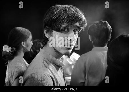 UN GIOVANE UOMO CHE GIRA INTORNO E GUARDA SERIAMENTE ALLA MACCHINA FOTOGRAFICA MENTRE IN UNA FOLLA Foto Stock