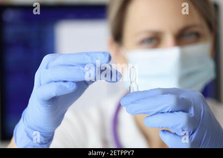 Infermiere in maschera e guanti che tengono la fiala di medicina closeup Foto Stock