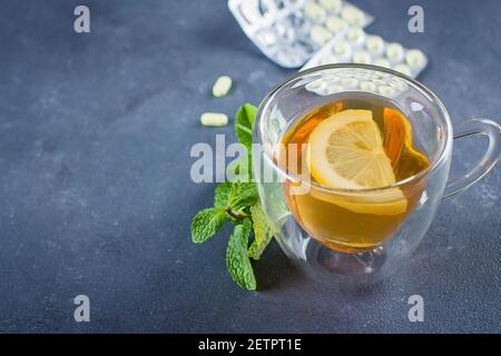 Medicinali, tazza di tè caldo e limoni con sfocato uomo malato sullo sfondo Foto Stock