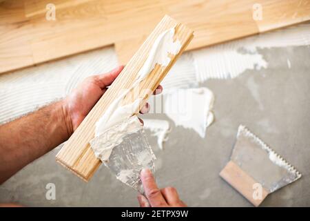 Applicazione manuale di colla per parquet su una piastra del pianale strumenti Foto Stock