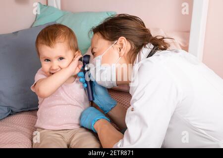 Il pediatra esamina l'orecchio della bambina a casa durante la quarantena pandemica del coronavirus COVID-19. Medico che usa otoscopio (auriscopio) per controllare il canale auricolare A. Foto Stock