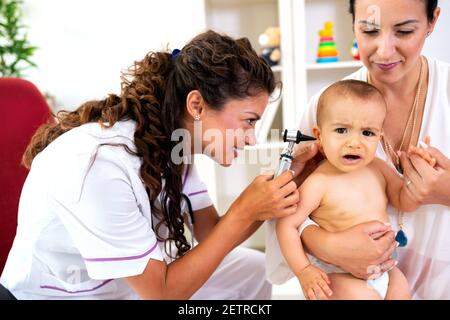 La madre amorevole che tiene il suo bambino come otologist esamina il suo bambino Foto Stock