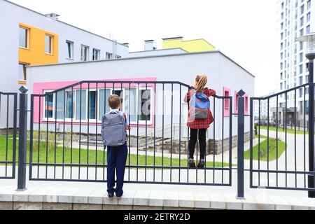 Bambini con borse portadocumenti sopra le spalle sullo sfondo della scuola. Foto Stock