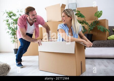 Felice festa giovane coppia acquisto nuovo appartamento, divertirsi e guidare con box attraverso la stanza Foto Stock