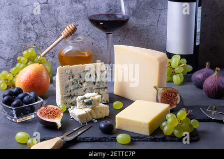 Formaggio blu e parmigiano su tavola nera, frutta, vino e miele. Primo piano. Foto Stock