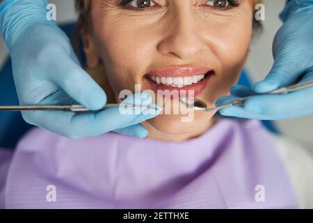 Mani che tengono la sonda dentale e lo specchio intraorale vicino ai denti della donna Foto Stock