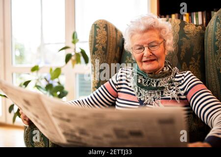 Anziana donna in pansion rilassarsi a casa mentre si legge un giornale Foto Stock