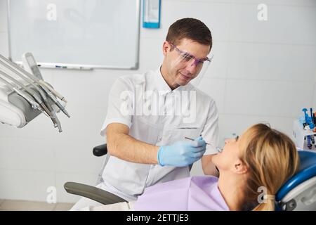 Medico amichevole in visiera che guarda all'interno della bocca della donna Foto Stock