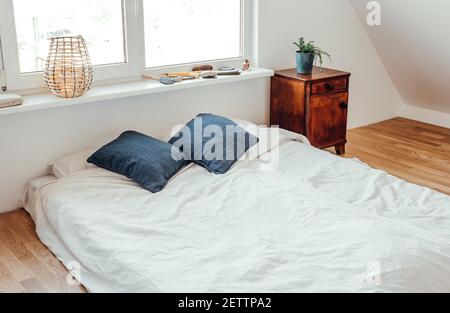 Materasso bianco minimalista sul pavimento in legno massiccio di quercia in una camera da letto accogliente e moderna. Camera luminosa e minimalista di colore bianco. Foto Stock