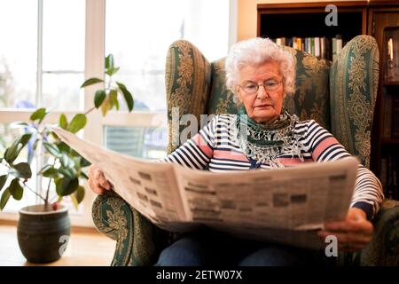 Anziana donna in pansion rilassarsi a casa mentre si legge un giornale Foto Stock