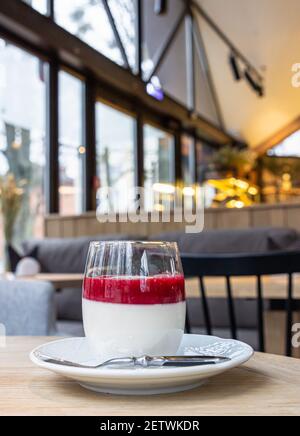 Delizioso dessert italiano panna cotta con salsa di frutti rossi su tavolo di legno, caffè sfondo interno. Messa a fuoco selettiva. Foto Stock