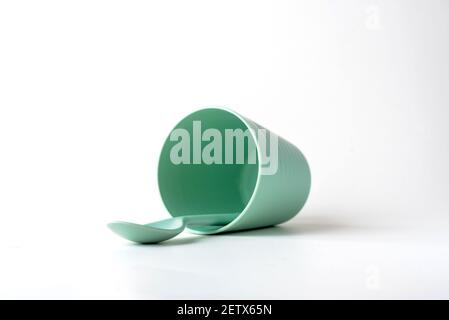Tazza di plastica e un cucchiaio isolato su sfondo bianco, le posate di plastica colorate verdi per bambini Foto Stock