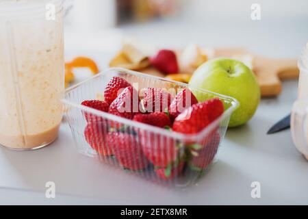 Fragole fresche in recipiente di plastica trasparente mela verde da tagliare e frullare in un frullato di frutta fresca. Foto Stock