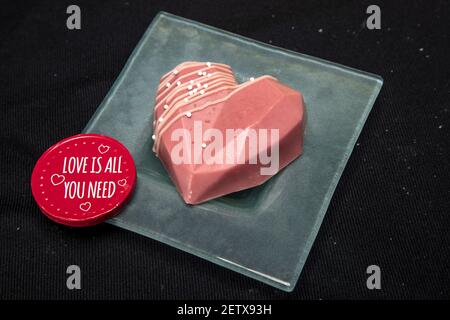 una bella cupcake a forma di cuore al cioccolato si trova su un piatto di vetro, isolato su uno sfondo nero Foto Stock