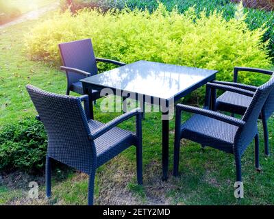 Tavolo con moderne sedie in rattan e tavolo da pranzo in vetro su erba verde nel giardino esterno. Foto Stock