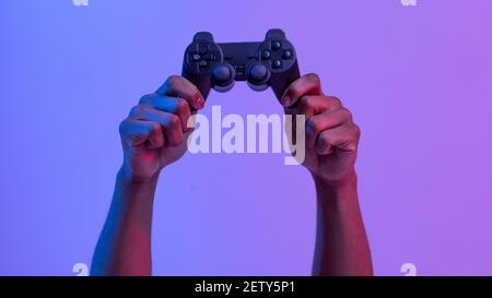 Mani nere maschio che tengono il joystick per i videogiochi su viola sfondo al neon Foto Stock