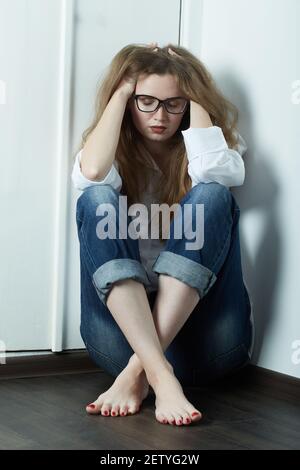 triste giovane donna in occhiali seduta sul pavimento guarda giù Foto Stock