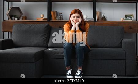 L'adolescente si è dispiaciuto guardando la fotocamera vicino allo smartphone sul divano Foto Stock