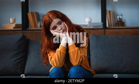 Dispiaciuto ragazza dai capelli rossi seduta sul divano in soggiorno Foto Stock