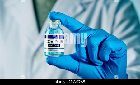 closeup di un operatore sanitario, indossando guanti chirurgici blu, con una bottiglia vaccinale covid-19 simulata in mano Foto Stock