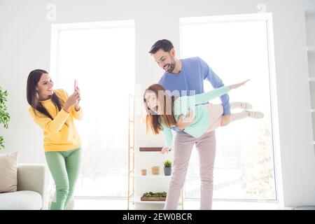 Ritratto fotografico di mamma che scatta foto di papà che tiene la figlia sulle mani che volano come l'aereo si è divertito a giocare a casa Foto Stock