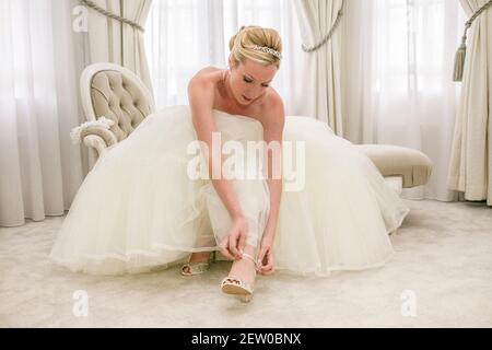 Sposa seduta sulla chaise lounge all'interno di muta nuziali il suo cinturino da scarpa Foto Stock