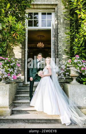 Sposa e sposo sposi nuovi in piedi sui gradini di pietra della casa padronale che hanno assunto per il giorno. Foto Stock