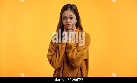 adolescente in maglione che pouda le labbra e le guance a contatto isolato su giallo Foto Stock