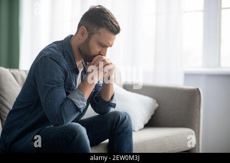 Uomo triste seduto sul divano a casa, vista laterale Foto Stock