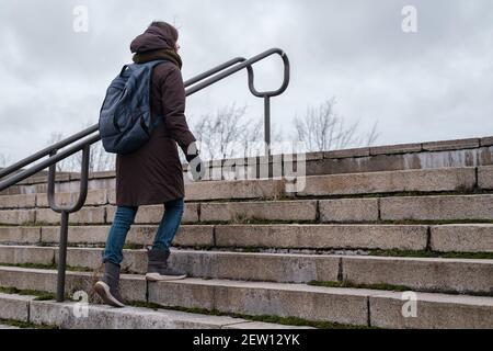 Un turista in abiti caldi e uno zaino in città sale i vecchi gradini in pietra delle scale in una giornata nuvolosa. Foto Stock