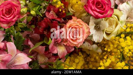 Composizione dei bordi dei fiori in colori giallo rosso brillante. Alstroemeria, rose, mimosa fiori. Vista dall'alto piatta, spazio per la copia Foto Stock