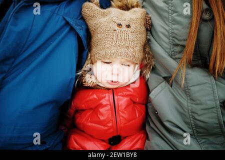 Concetto di cura parentale, ritratto di carino infelice triste ragazza in vestito caldo seduta tra i suoi genitori in inverno Foto Stock