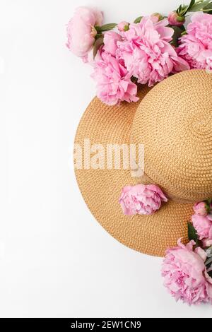 Estate, concetto di primavera, cappello intrecciato in paglia, fiori di pony rosa su sfondo bianco, vista dall'alto Foto Stock