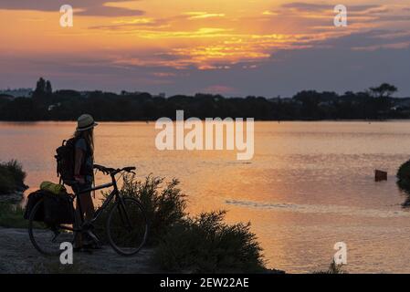 Francia, Gard (30), Aigues-Mortes, giovane donna che contempla il tramonto di fronte all'Etang du Médard Foto Stock