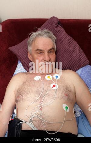 Uomo con un monitor holter sdraiato sul divano Foto Stock