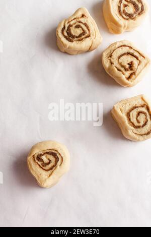 Fette di pasta cruda di rotoli di cannella su uno sfondo bianco di carta da forno. Foto Stock