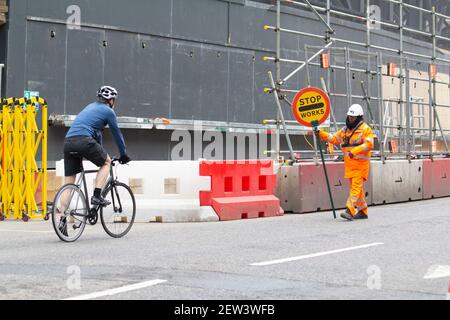 Un Marshall del traffico tiene in su il segno di arresto per arrestare una città solitaria del ciclista in arrivo di Londra, durante il lockdown Pandemic di Coronavirus Covid-19 Foto Stock
