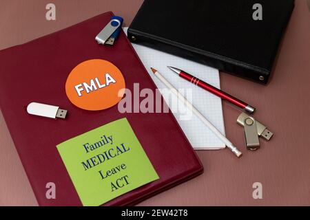 FMLA Family and Medical Leave Act. Sul tavolo da ufficio c'è un grande notebook rivestito in pelle, una matita, una penna e delle schede per la memorizzazione delle informazioni. M Foto Stock