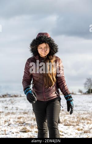 Una ragazza adolescente in una giacca invernale con cappuccio in un freddo paesaggio invernale. Neve e un cielo nuvoloso sullo sfondo Foto Stock