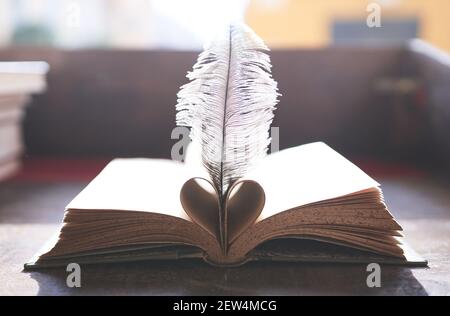 Aprire il libro con le pagine piegate a forma di cuore e una piuma tra loro su tavola di legno Foto Stock