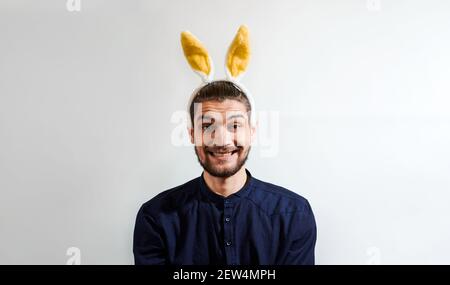 Giovane affascinante con barba in camicia con costume da coniglietto pasquale. Uomo con orecchie di coniglio. Persom con orecchie di lepre sorride grande sorriso. Banner creativo per Foto Stock