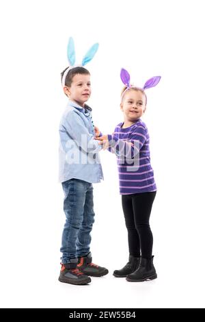 Adorabile giovane ragazzo e ragazza abbracciano con orecchie di coniglietto pasquale. Corpo intero isolato su sfondo bianco. Foto Stock