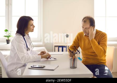 Medico che ascolta i pazienti anziani di sesso maschile che lamentano mal di testa, stress e affaticamento Foto Stock