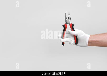 Mano dell'uomo in guanto bianco rialzato con un utensile nero e rosso: Pinze, tagliafili. Isolato su sfondo bianco. Aprire, pulire, pronto per il taglio. Simulazione Foto Stock