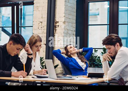 La donna d'affari si rilassa mentre i suoi colleghi lavorano Foto Stock