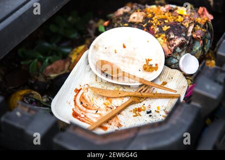 Set di piastre a balestra di palma usate sporche e biodegradabili e forchetta, coltello, cucchiaio all'interno del bidone compost per il compostaggio. Stoviglie perfette per il giardino. Foto Stock